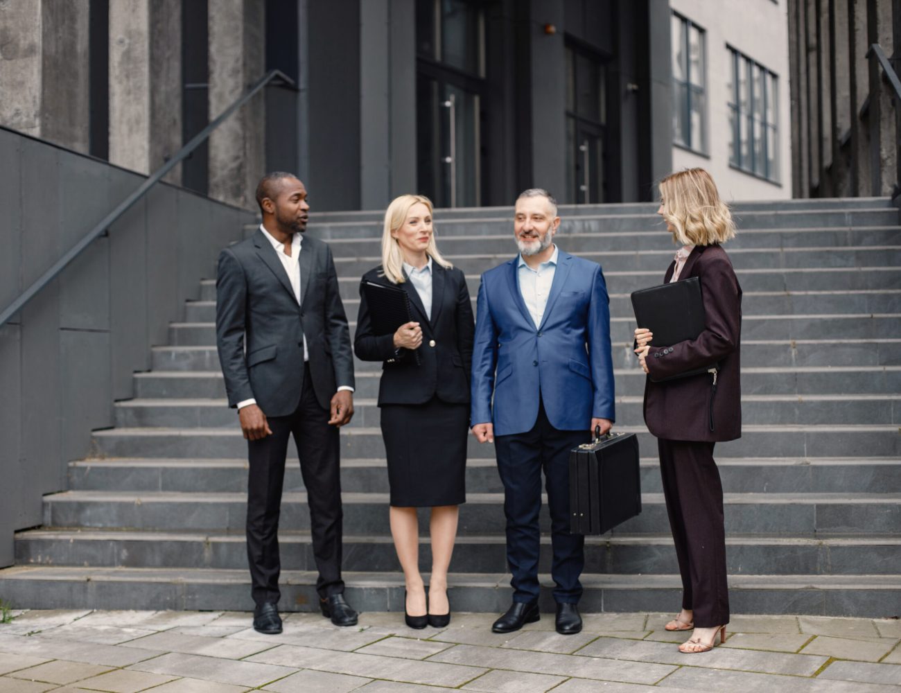 Confident businesspersons standing in front of modern office building. Men and women talking and holding documents. Banking and financial market concept.